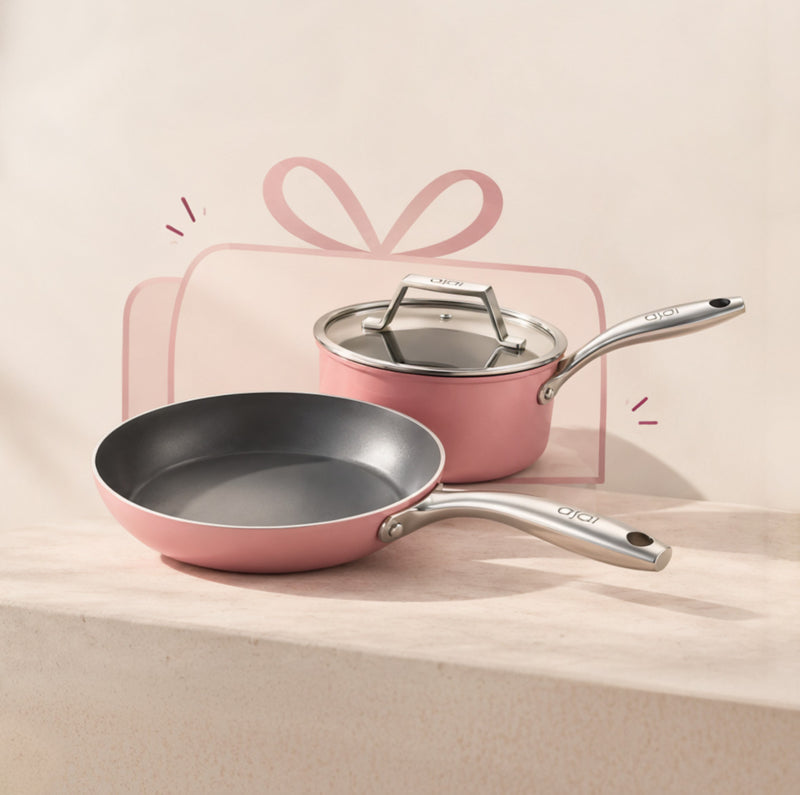 Pink Asai frying pan and sauce pan in front of a gift ribbon.